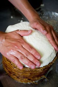 To remove excess whey, a cheese maker gently presses the salted curds in a basket.