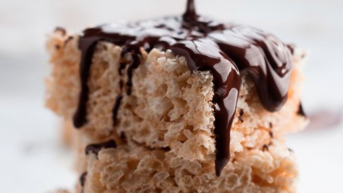 A cascade of rich chocolate being drizzled over a stack of Rice Krispies.