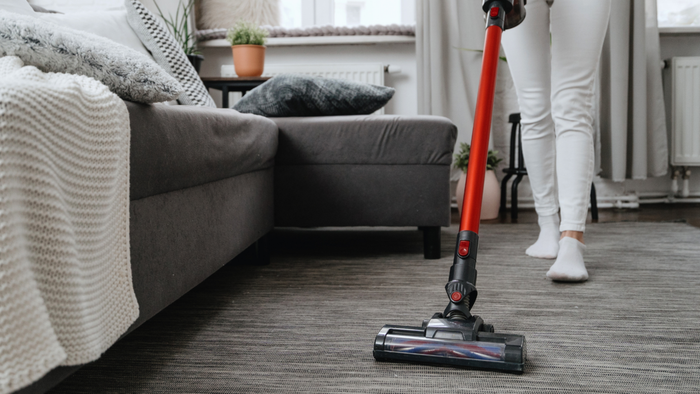 A mid-shot of a person using a stick vacuum to clean a carpeted floor