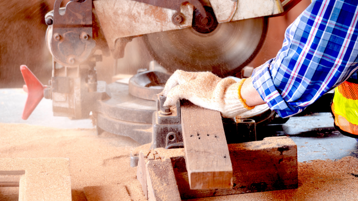 A person using a miter saw to cut wood, with sawdust scattered around the workspace