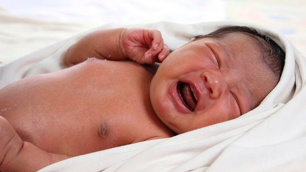 A newborn infant swaddled in a white blanket, crying