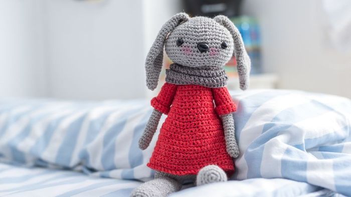 A vibrant red knitted doll rests comfortably on a bed.