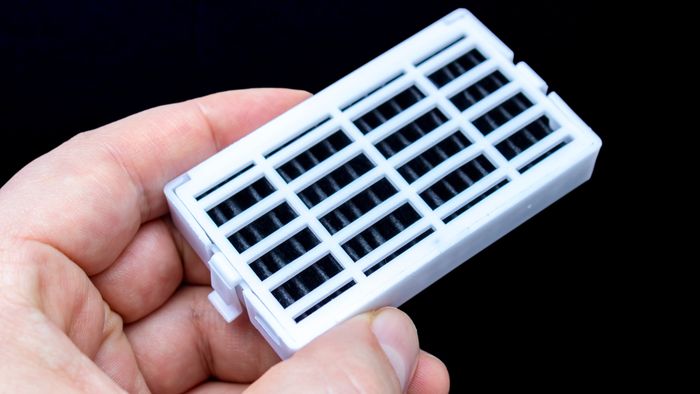 A person’s hand holding a white air filter for the refrigerator