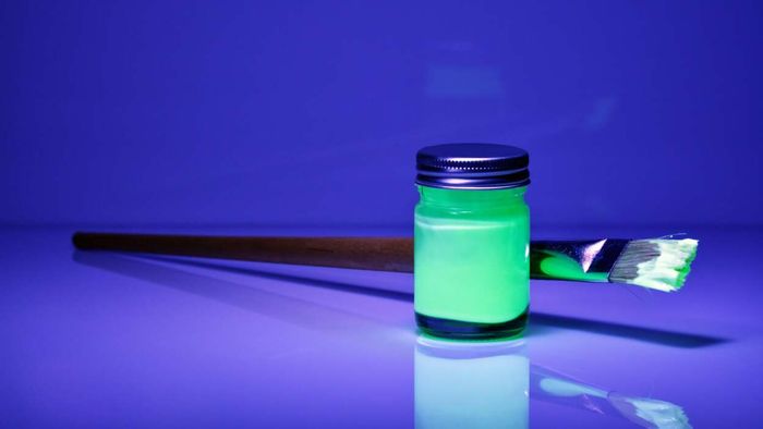 A glowing green paint bottle illuminated under a blacklight