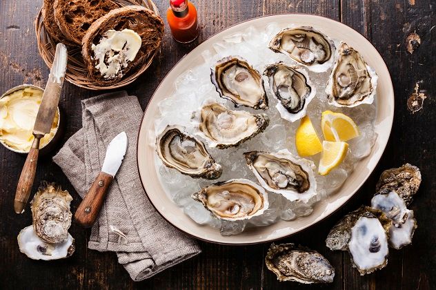 Opened oysters on a plate with dark bread and butter, set against a dark wooden background