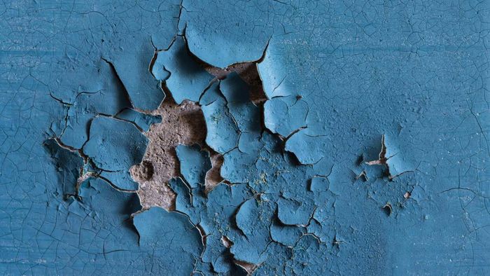 A concrete wall with blue paint that’s peeling and forming blisters