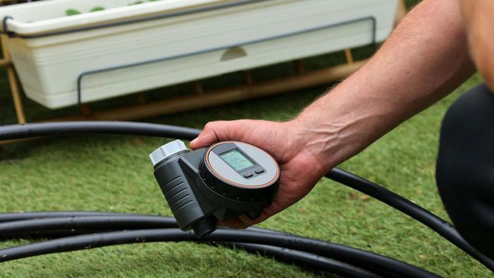 A person holding a smart hose timer in their yard