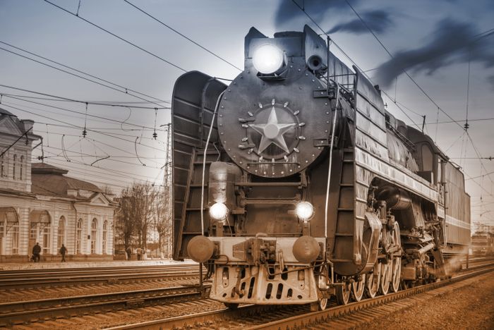 A vintage steam train is stationed at the platform during the evening.