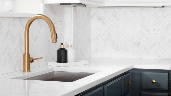 A kitchen sink featuring a sleek, modern brass arched faucet
