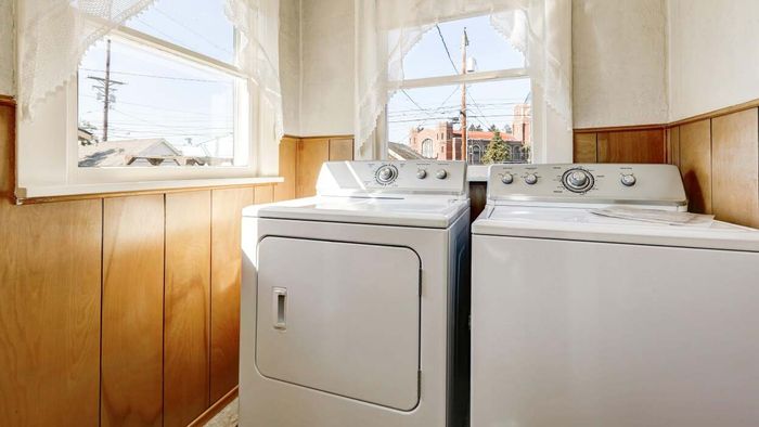 A vintage laundry room with wooden panels housing older white washer and dryer units