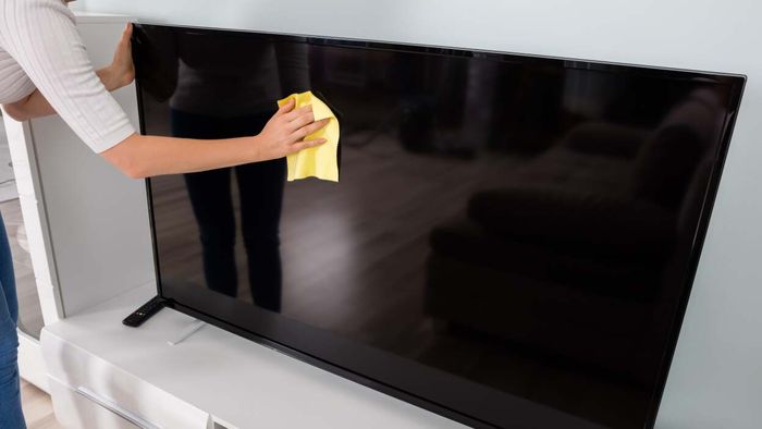 A woman cleaning a television screen using a cloth