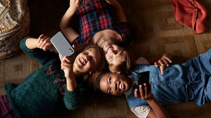Three teens relaxing on the ground, engrossed in their smartphones.