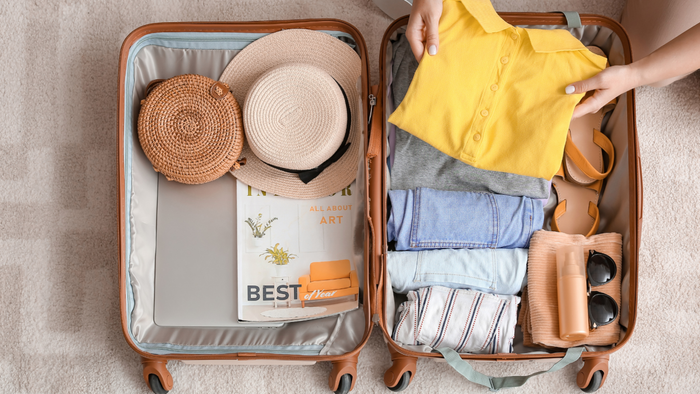 a person organizing summer clothes and accessories inside a suitcase