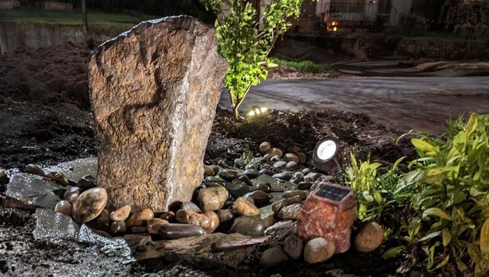 A large rock bubbler in a yard, illuminated by solar-powered lights designed to resemble rocks on either side.