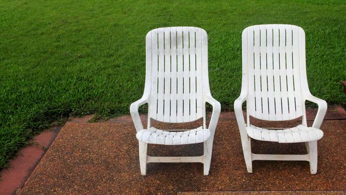 A pair of aged, scratched, and grimy white plastic lawn chairs