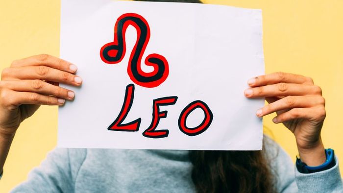A young woman holding a hand-drawn Leo zodiac symbol on paper.