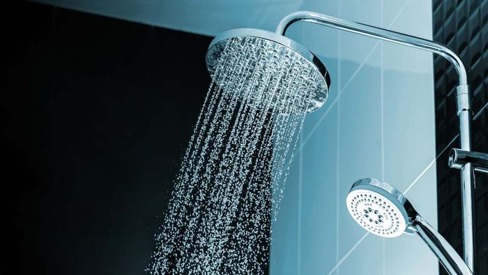 A circular waterfall-style showerhead disperses water against a backdrop of light blue tiles.