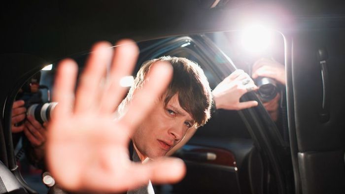 A famous figure shielding his face from the relentless glare of camera flashes.