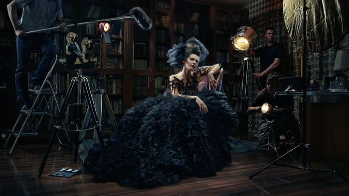 A woman dressed in vintage attire, seated on a chair within a film studio setting.