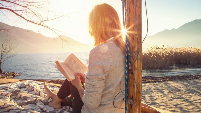 A young woman enjoying a peaceful moment by a lakeside, engrossed in a captivating book.