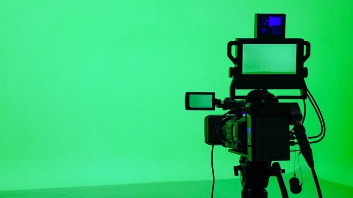 A camera positioned in front of a vibrant green backdrop.