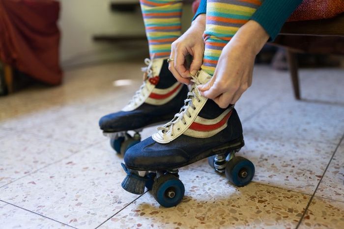 A close-up of a woman’s hands tying the laces of vintage roller skates over colorful striped socks.
