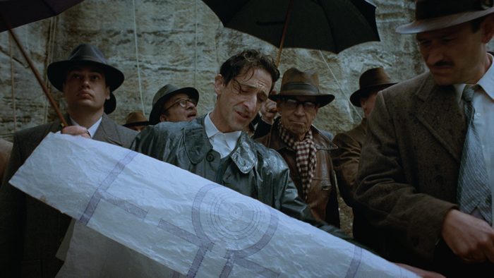 A scene from The Brutalist depicting Adrian Brody examining a blueprint for a circular structure