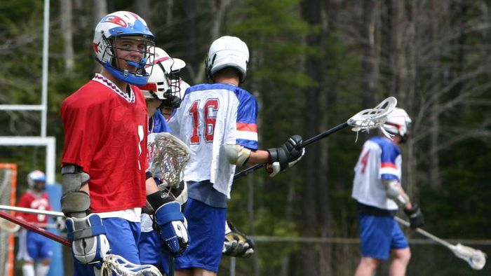 A high school lacrosse player stands alongside his teammates on the field, ready for action.