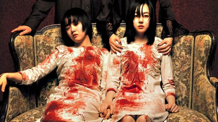 A still from A Tale of Two Sisters shows two bloodied sisters seated on a couch.