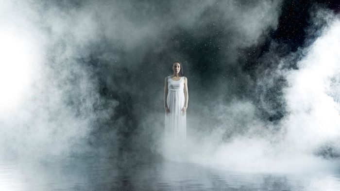 A female performer on a stage enveloped in a misty fog.
