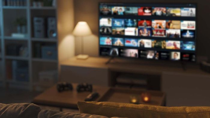 A dimly lit living room with a blurred smart TV screen showcasing various unrecognizable apps