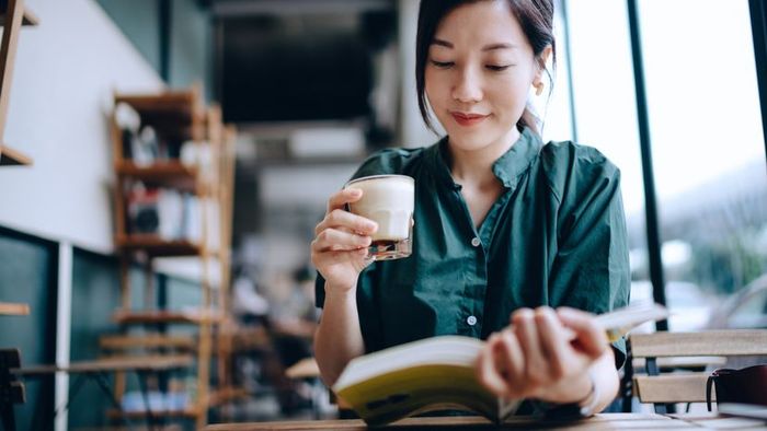 A young woman enjoys a peaceful moment, sipping coffee and reading a book at a cozy cafe.