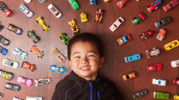 A young boy sprawled on the floor, surrounded by a collection of miniature toy cars.