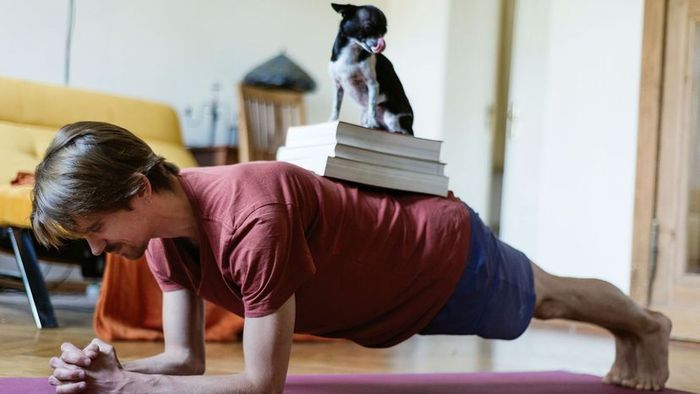 A man performing planks alongside a dog and a book