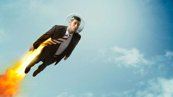 A man dressed in a suit soaring through the air using a jetpack.