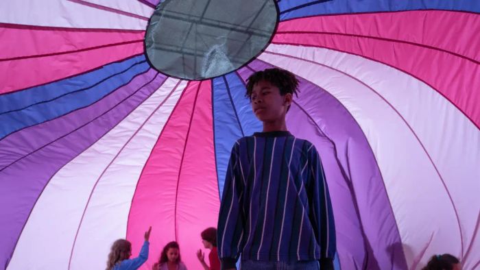 A scene from I Saw the TV Glow features a character beneath a vibrant canopy of purple, pink, and blue hues.