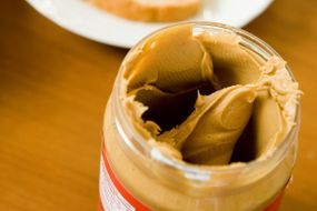 A jar of peanut butter opened next to a slice of breakfast toast
