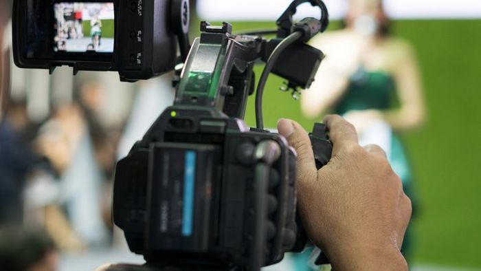 A man capturing footage of a TV presenter.