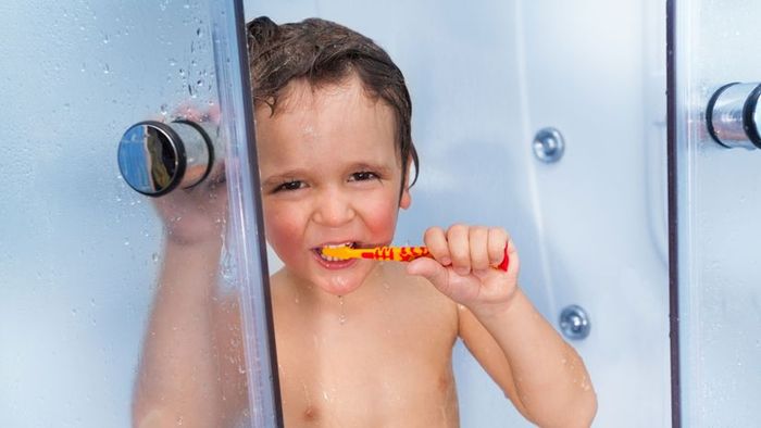 child holding a toothbrush in the shower