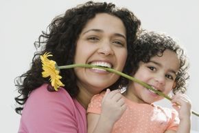 A mother and daughter holding a flower between their teeth.