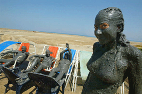 A visitor to the Dead Sea applies revitalizing mud before immersing herself in the renowned waters.