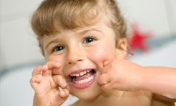 A young girl carefully flosses her teeth.