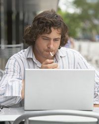 A young man smoking while using a laptop
