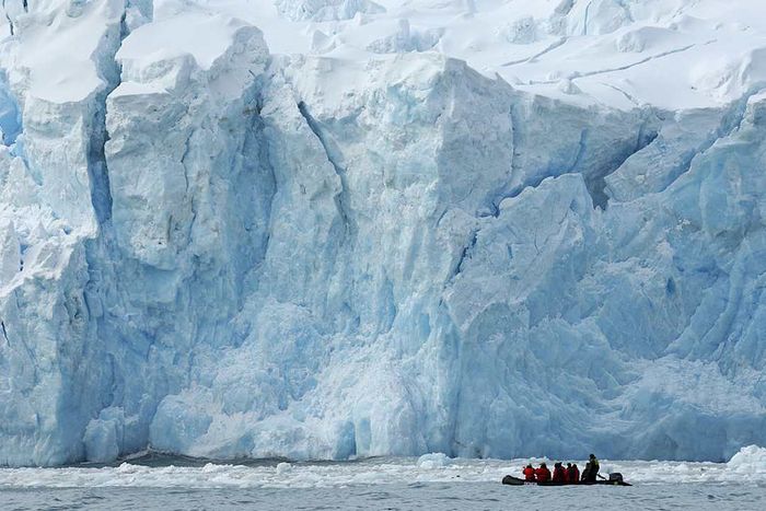 Tourists examine a glacier from an inflatable Zodiac boat