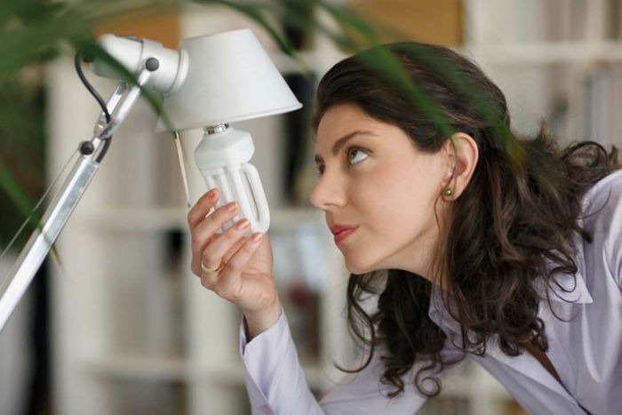 A woman replacing a traditional bulb with a CFL bulb.