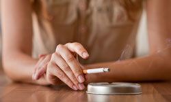 A woman's hand holding a cigarette next to an ashtray