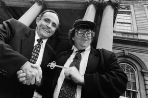 In 1994, Mayor Rudy Giuliani and filmmaker Michael Moore stand in front of a building, shaking hands and holding a ceremonial key.