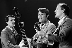 A monochrome photograph captures three musicians performing together in the early 1960s.
