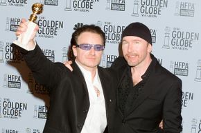 Musician Bono holds an award while standing beside The Edge, another musician.