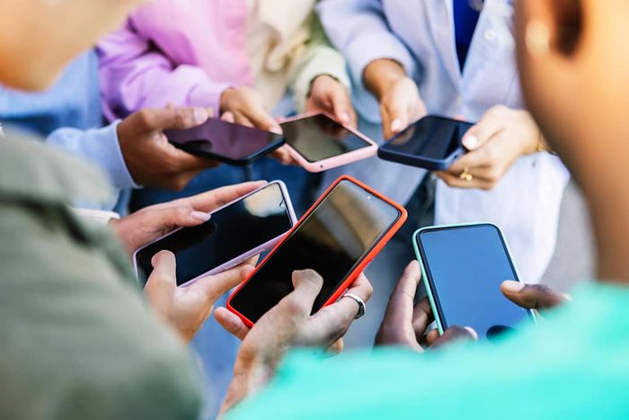 A group of young individuals standing in a circle, using their mobile phones outdoors.
